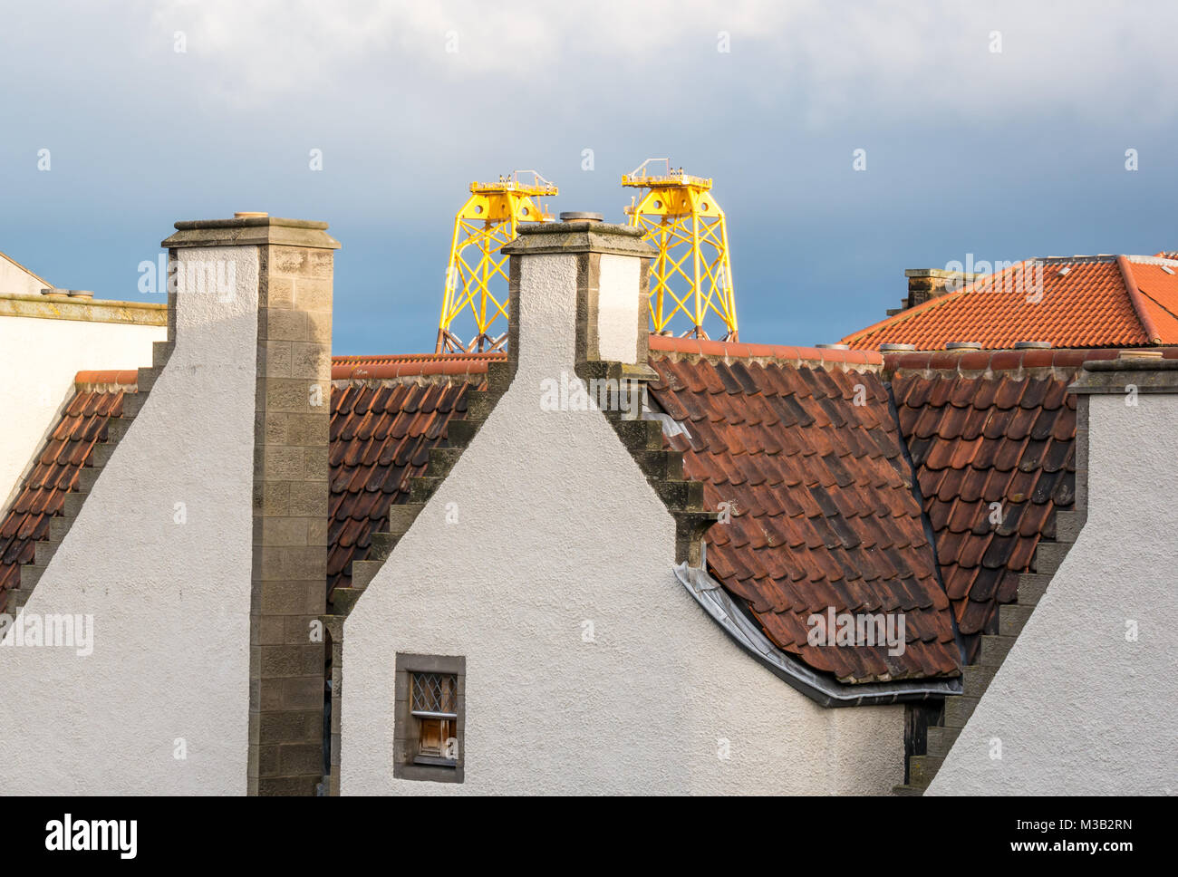 Leith, Edimburgo, Scozia, Regno Unito. Incongrua giustapposizione di enorme giallo sole turbina eolica piattaforme, chiamato giacche per centrali eoliche, in Leith Harbour che torreggiano sulla pantile tetto di uno degli edifici più antichi di Leith, xvii secolo agnello della casa di un ex Hanseatic Leith Merchant House, ora casa per l'architetto che ha ripristinato, Nicholas Groves Raines. Queste piattaforme di arrivare in Leith sul loro modo Nord per fornire una struttura secondaria per le turbine in un offshore wind farm in Moray Firth Foto Stock