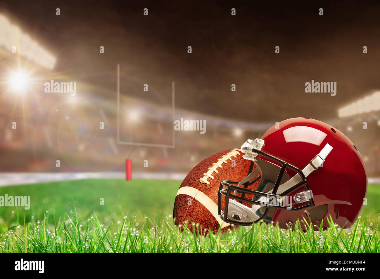 Il football americano casco e la palla sul campo in erba luminosamente illuminata outdoor stadium con focus sul primo piano e profondità di campo sullo sfondo. De Foto Stock
