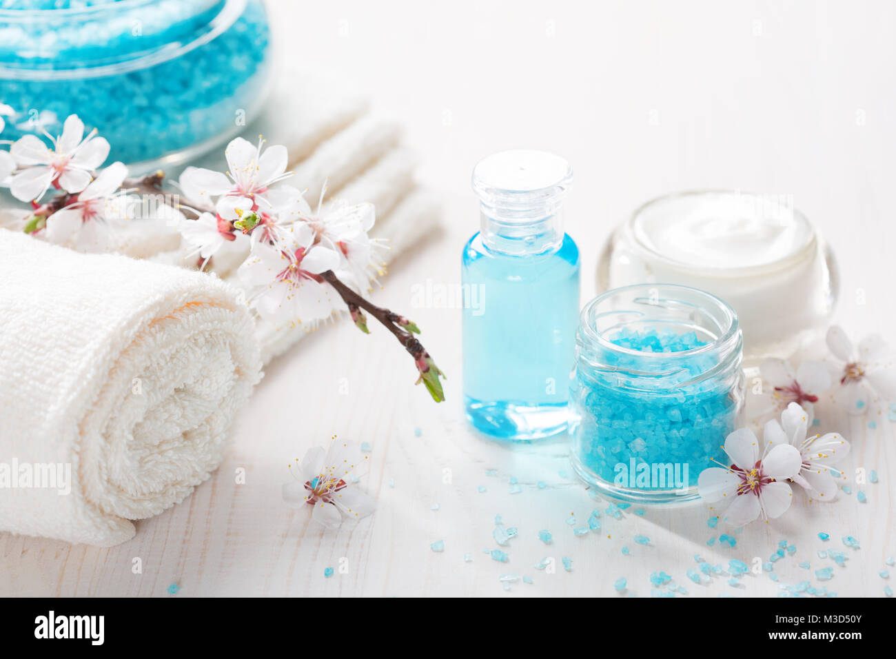 Bagno minerale sali, crema, gel doccia, asciugamani e fiori sul tavolo di legno. DOF poco profondo. Focus sul sale. Foto Stock