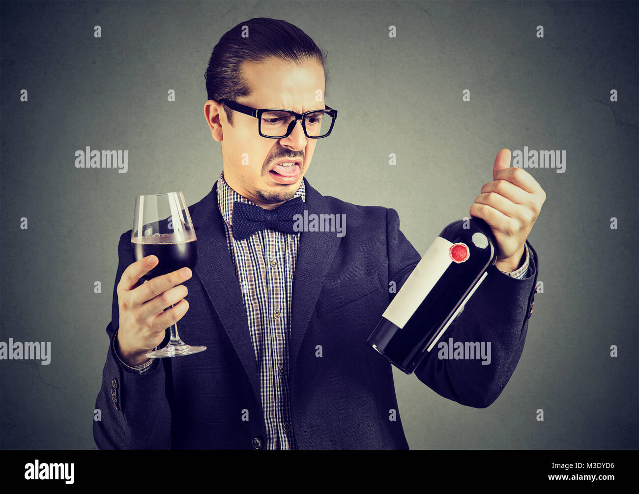 Giovane uomo formale cercando grumpy durante la degustazione del vino rosso e per esplorare la bottiglia. Foto Stock