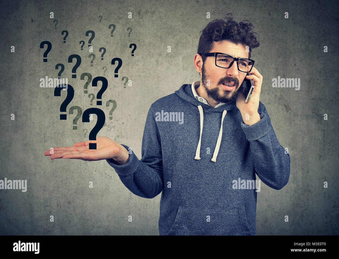 Giovane uomo barbuto parlando sullo smartphone in malintesi su sfondo grigio. Foto Stock