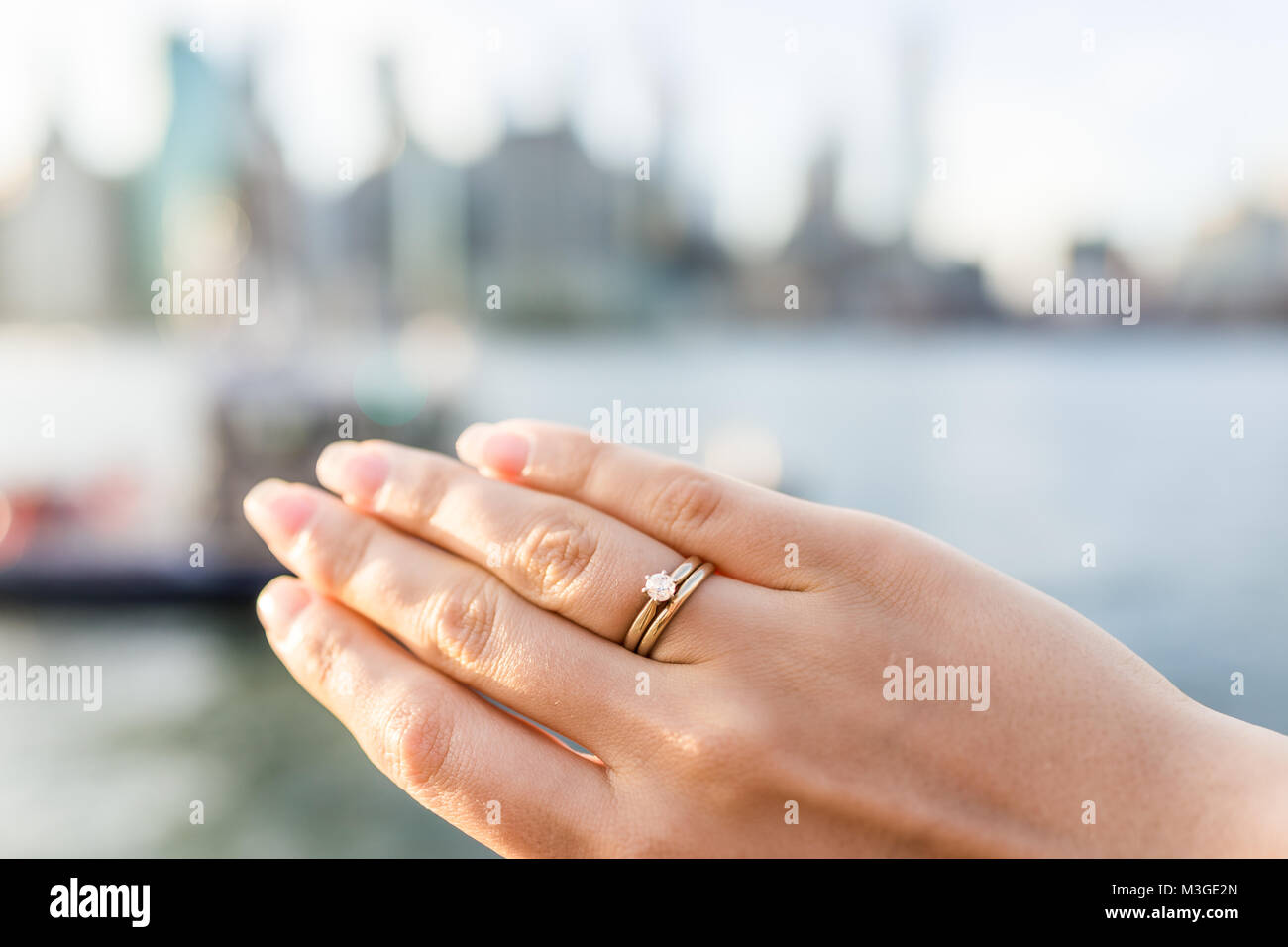 Giovane donna la mano con diamante anello di fidanzamento solitario, oro  wedding band fuori all'aperto in NYC New York City Ponte di Brooklyn Park  da East River Foto stock - Alamy