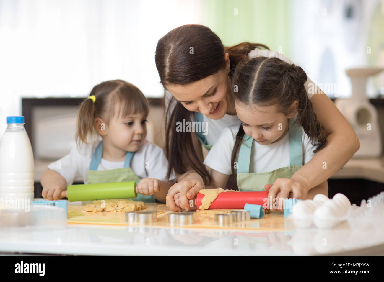 Carino bambini piccoli e il loro bellissimo Mamma in grembiuli sono la riproduzione e ridere mentre impastare la pasta in cucina Foto Stock