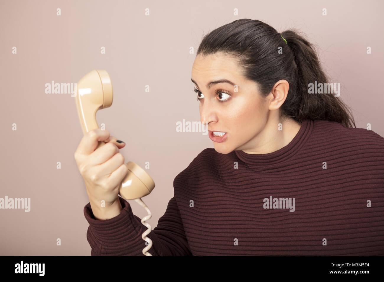 Arrabbiati arrabbiati donna digrignando i denti e ululano al ricevitore telefonico lei tiene in mano Foto Stock