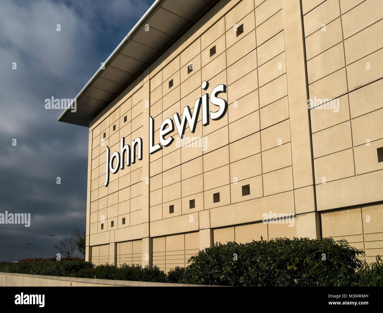 Large White John Lewis shop logo del marchio sul soleggiato parete esterna di The Mall at Cribbs Causeway con nuvole scure in distanza, Bristol, Inghilterra, Regno Unito Foto Stock