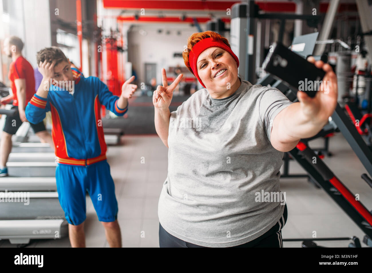 Donna grassa rende selfie con istruttore in palestra, umorismo. Calorie bruciare, femmina obesi in persona lo sport club, fat-burning Foto Stock