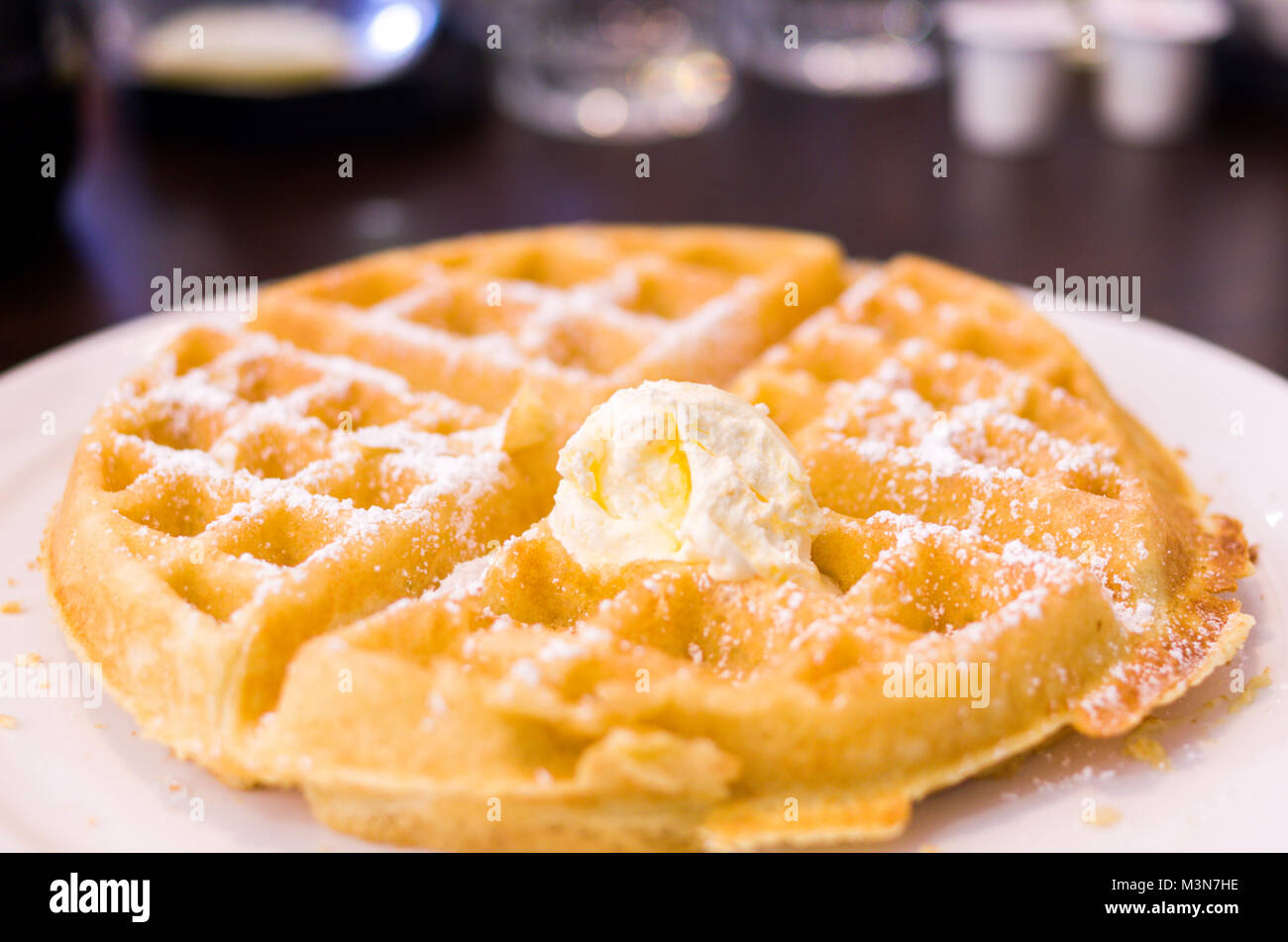 La colazione waffle conditi con burro e spolverate con zucchero a velo. Un tradizionale primo pasto favorito meglio serviti caldi con sciroppo di acero. Foto Stock
