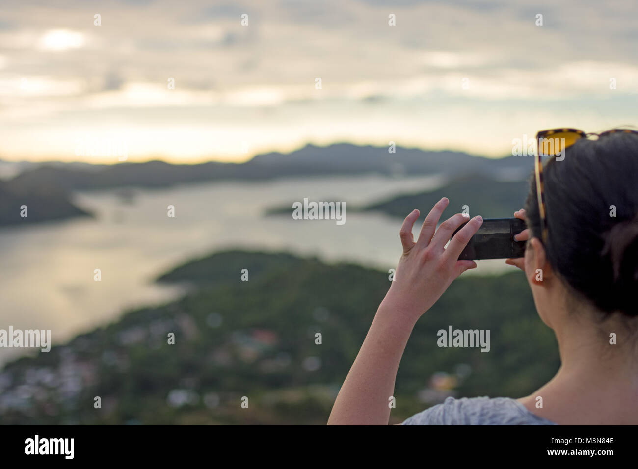 Dai capelli scuri donna prendendo uno smart phone foto in una vista in elevazione del mare e delle isole intorno Coron, PALAWAN FILIPPINE. Foto Stock