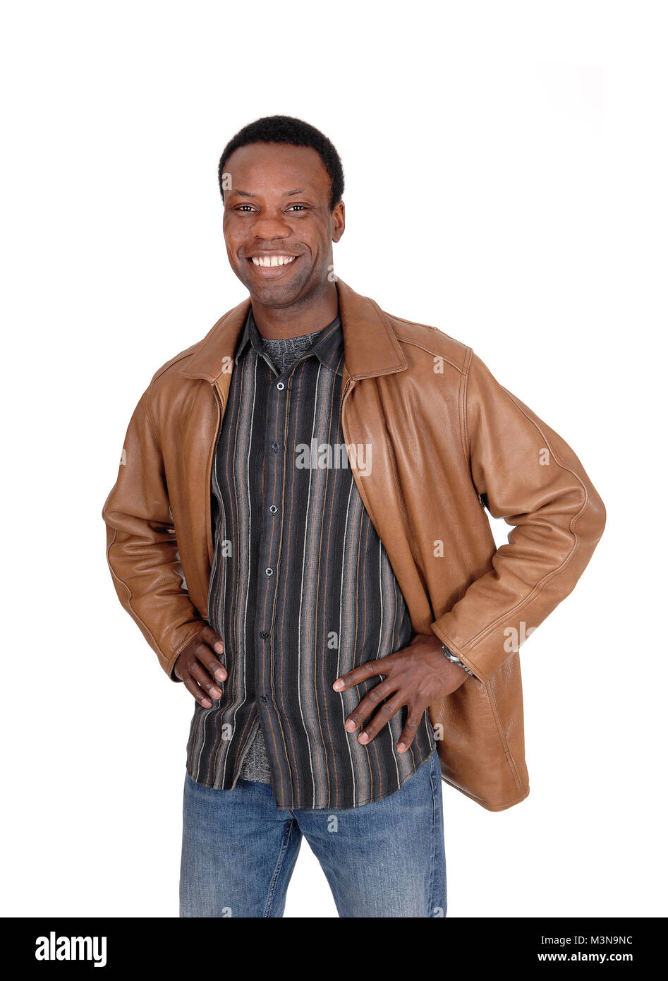Un bel giovane americano africano uomo sorridente in una giacca di pelle marrone con le mani sui suoi fianchi, isolato per sfondo bianco Foto Stock