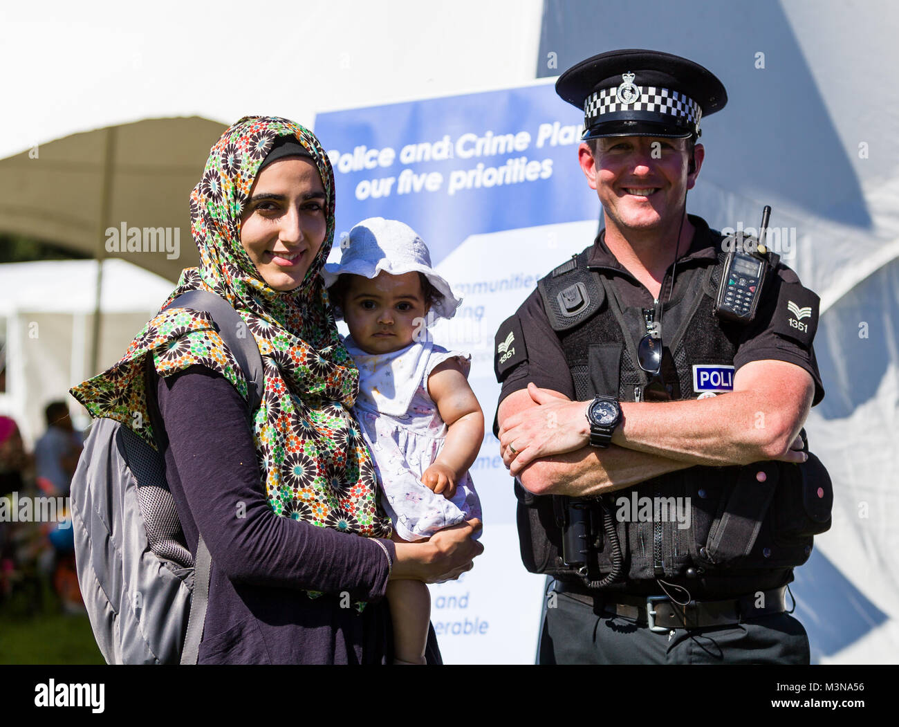 Un funzionario di polizia e una donna musulmana con un bambino di stare di fronte ad un crimine prevenzione banner. Foto Stock