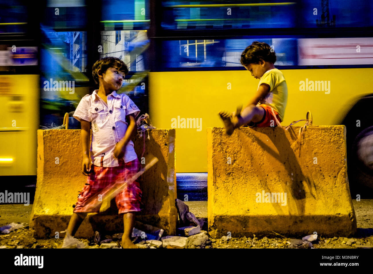 Bambini da sporti giocando vicino a traffico di notte lungo la strada in Città Vecchia Yangon Myanmar Foto Stock