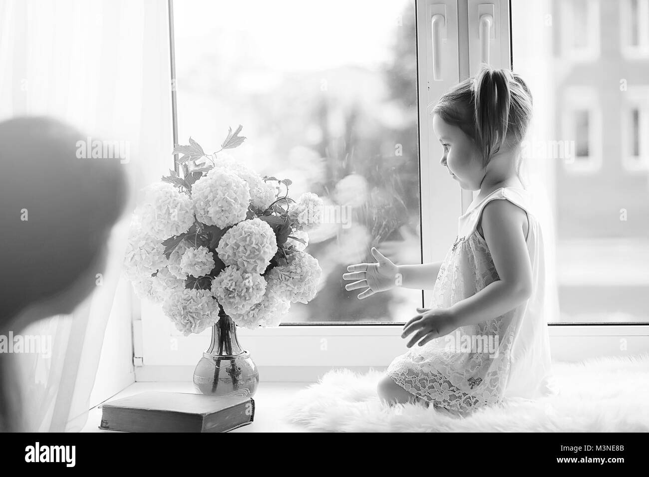 La bambina è seduta sul davanzale. Un mazzo di fiori Foto Stock