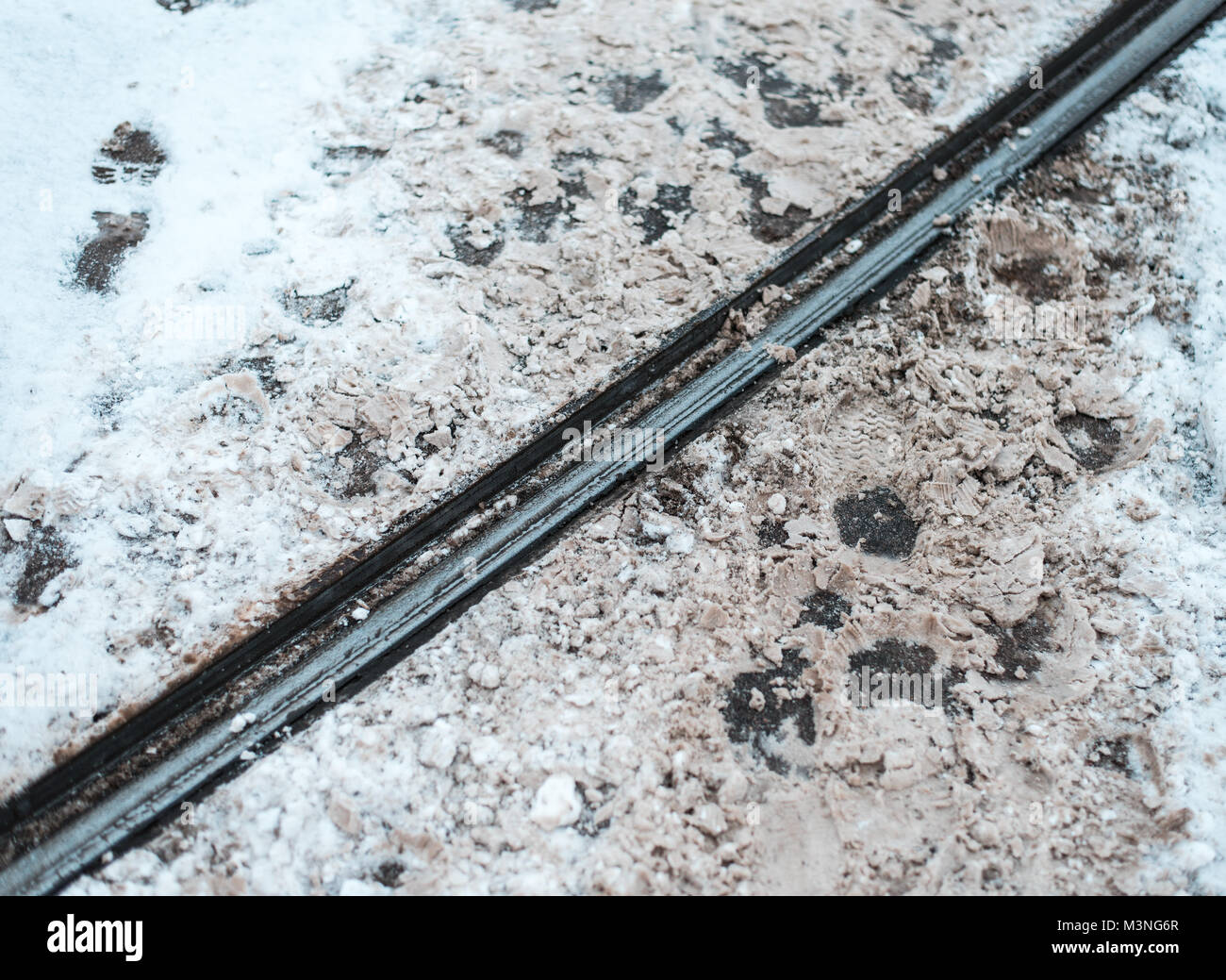 Biglietto del tram in inverno nella città. Orme di pedoni che attraversano i binari di metallo dello sfondo. Foto Stock