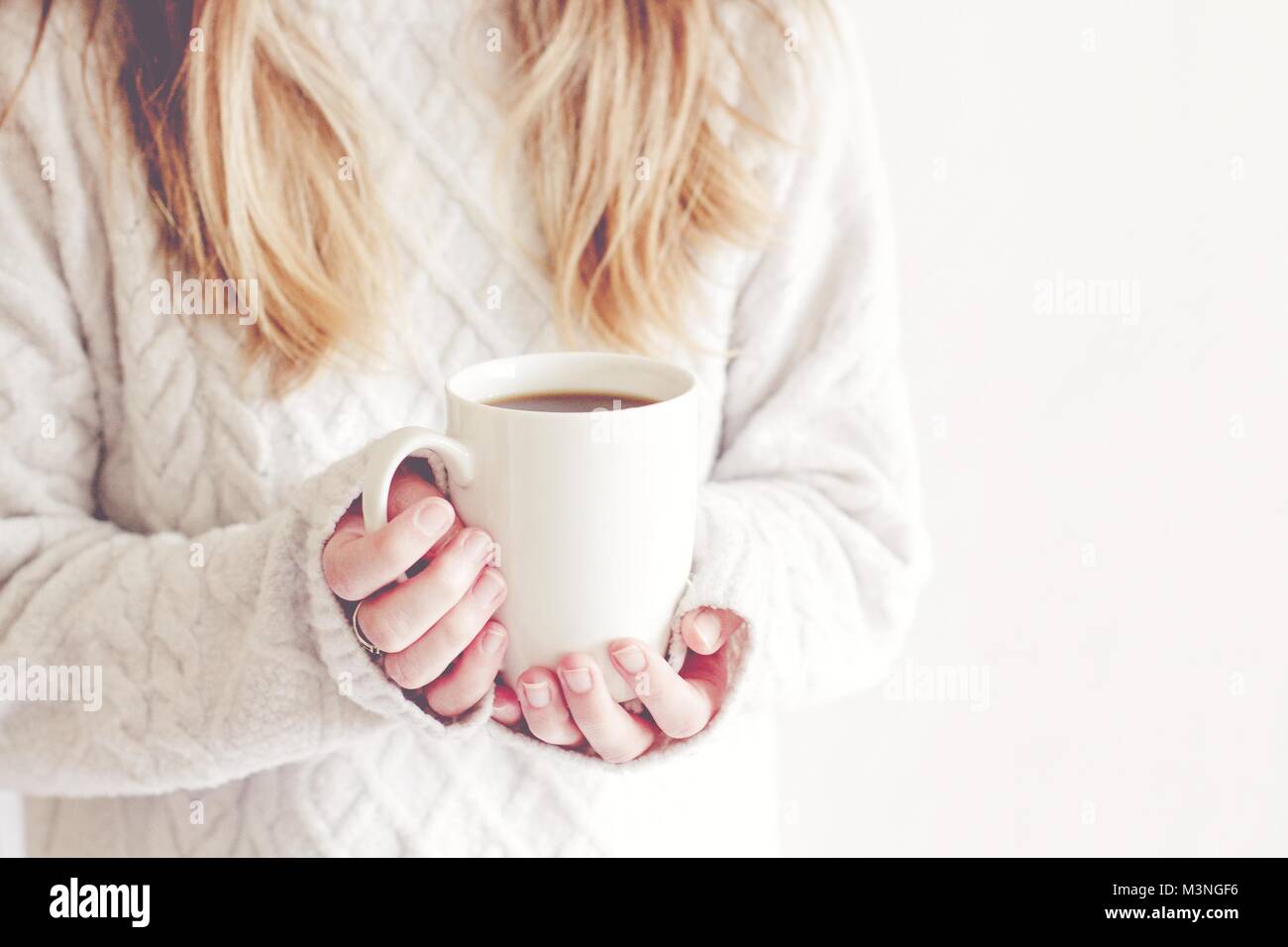 Una sezione mediana di una bionda ragazza dai capelli con in mano una coppa di bianco isolato su un fondo bianco in un accogliente stile di vita dell'immagine. Foto Stock