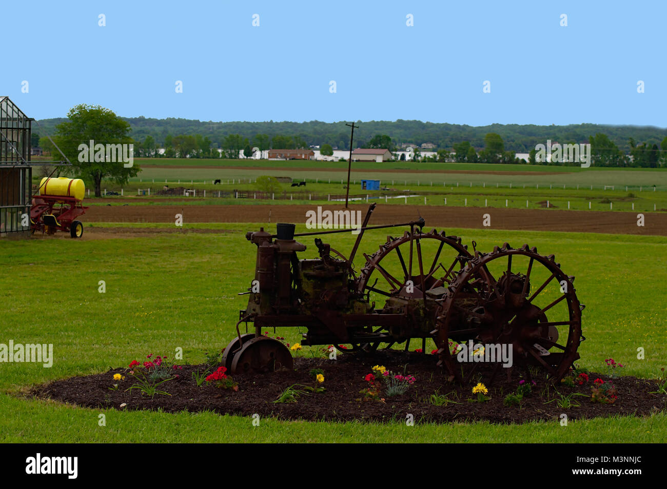 Antico trattore nel letto di fiori con fiori rossi e gialli Foto Stock