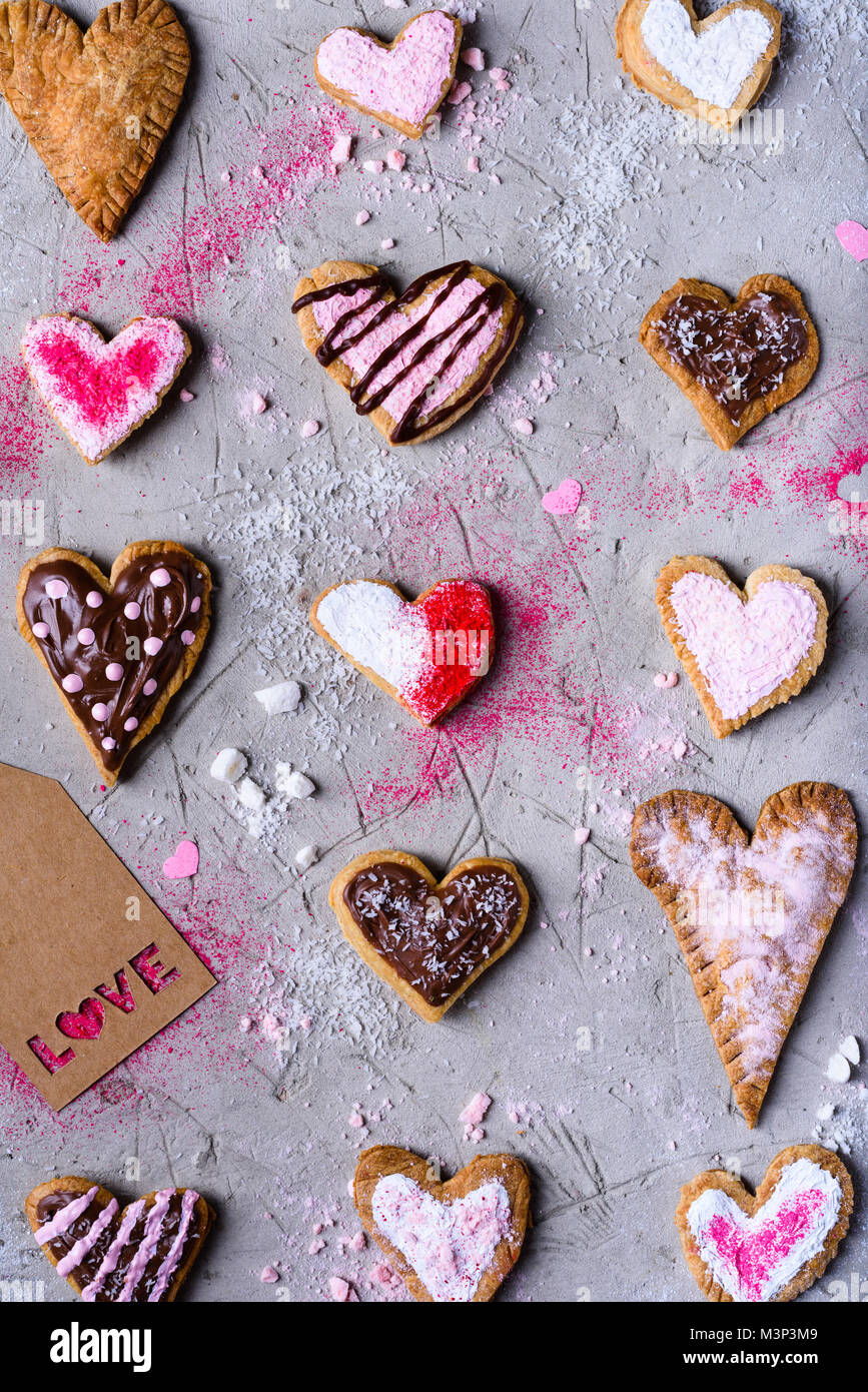Vista dall'alto di diversi a forma di cuore i cookie con amore tag grigio sulla superficie incrinato Foto Stock