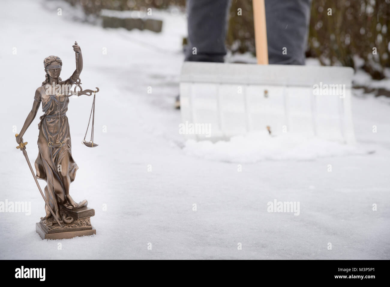 Quando dovete cancellare la neve? - Justitia statua in primo piano e sullo sfondo di un uomo è la rimozione di neve fuori sul marciapiede Foto Stock