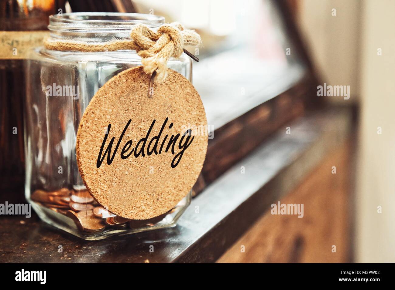 Vintage retrò vasetto in vetro con corda di canapa tie tag di nozze e le poche monete all'interno di legno sul concetto di contatore di risparmio di denaro per matrimoni Foto Stock