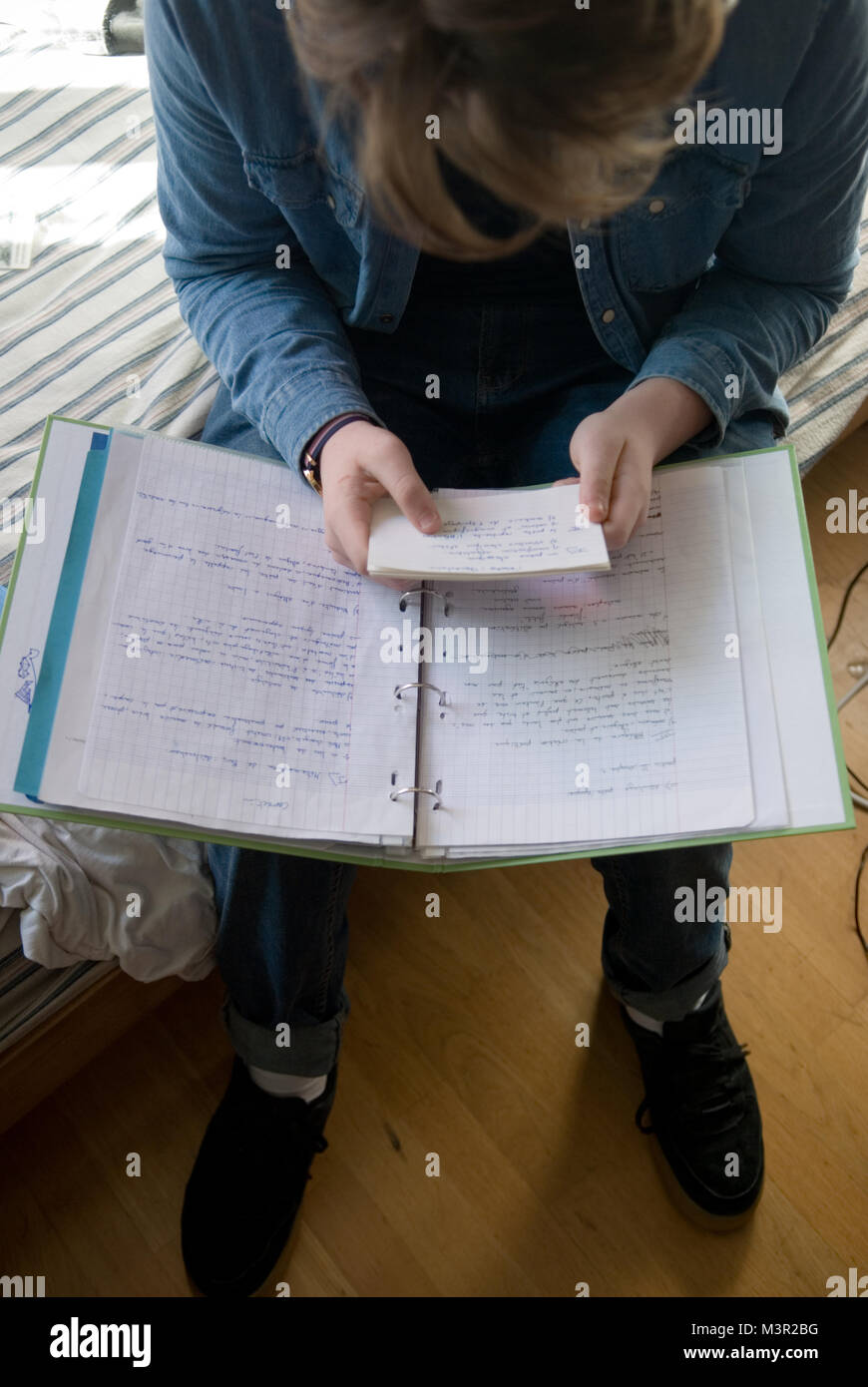 Guardando verso il basso a caucasian francese adolescente di sesso maschile seduto sul suo letto rivedendo le sue note per un esame Foto Stock
