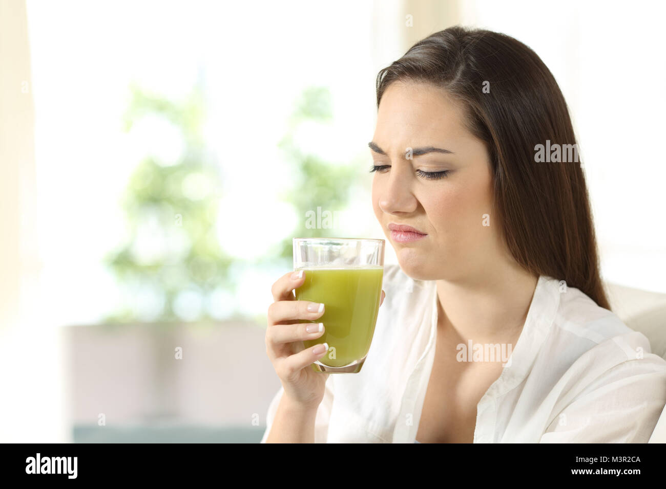 Disgustato donna per degustare un succo vegetale con sapore cattivo seduta su un divano nel salotto di casa Foto Stock