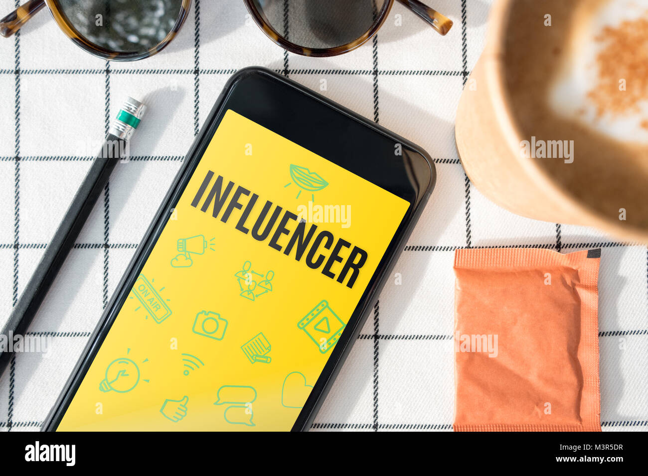 Vista superiore influencer funzione sulla schermata mobile con tazza di caffè,occhiali da sole,matita sul tavolo bianco panno.blogger lifestyle. Foto Stock