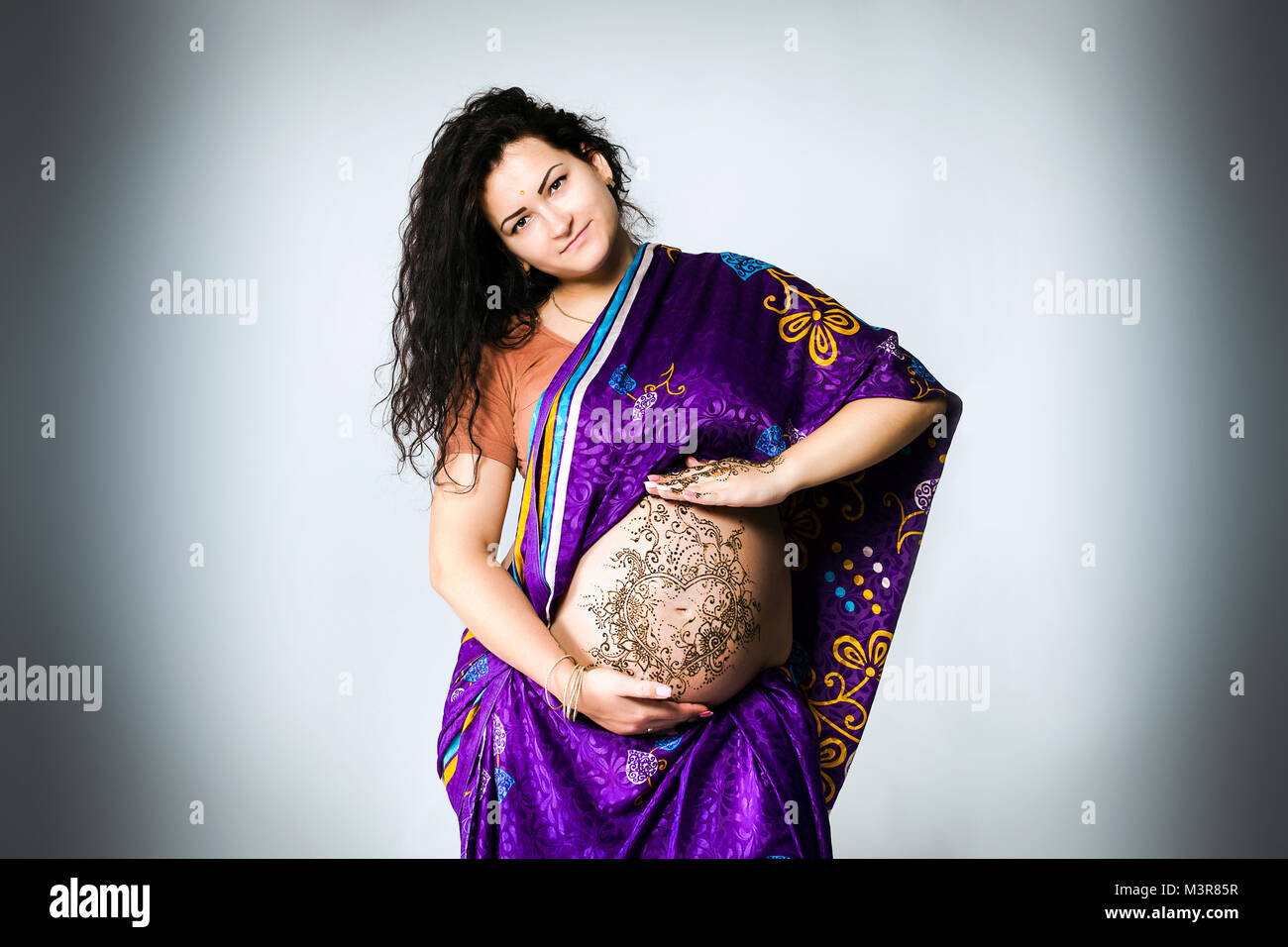 Studio ritratto di una donna in stato di gravidanza in Indian sari, una gravidanza pancia dipinta con henné Foto Stock