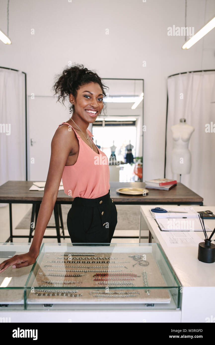Femmina designer di moda in piedi alla sua scrivania nella sua boutique. Sorridente abito femminile designer nel suo negozio di stoffa. Foto Stock