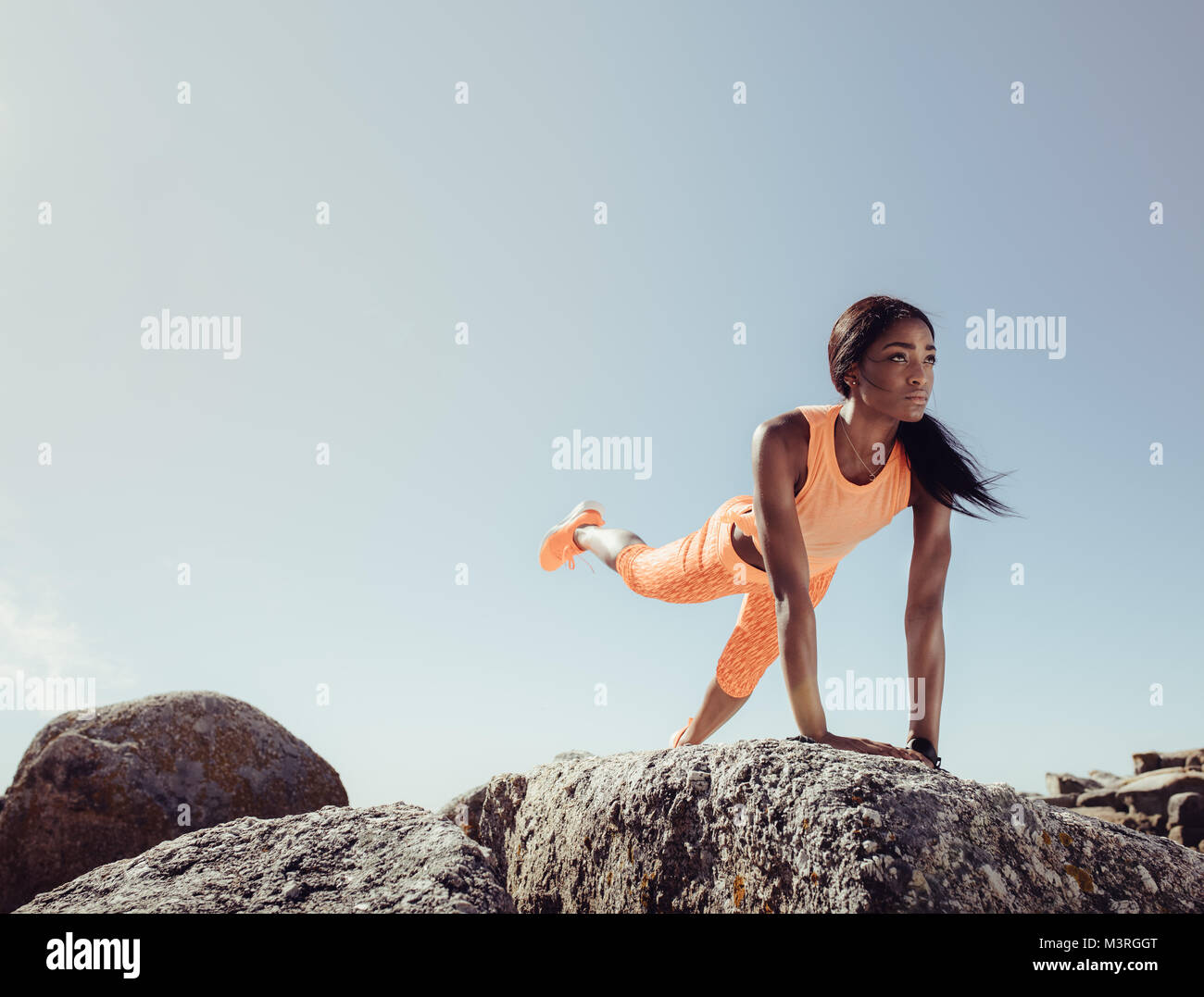 Femmina nero facendo esercizi di stretching sulle rocce in spiaggia su una mattina d'estate. Montare donna stretching la sua gamba alla spiaggia. Foto Stock