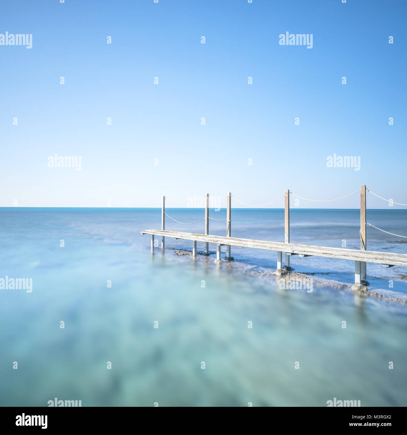 Passerella in legno o passerella e banister sull'acqua di mare. Fotografia a lunga esposizione. Foto Stock