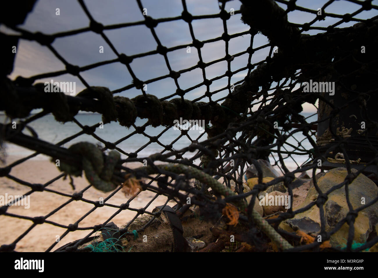 Chiusura del vecchio, scartato lobster pot abbandonati sulla spiaggia, tra i detriti si è incagliata dalla marea. Soft-focus Tramonto Tramonto, visibile attraverso la rete. Foto Stock