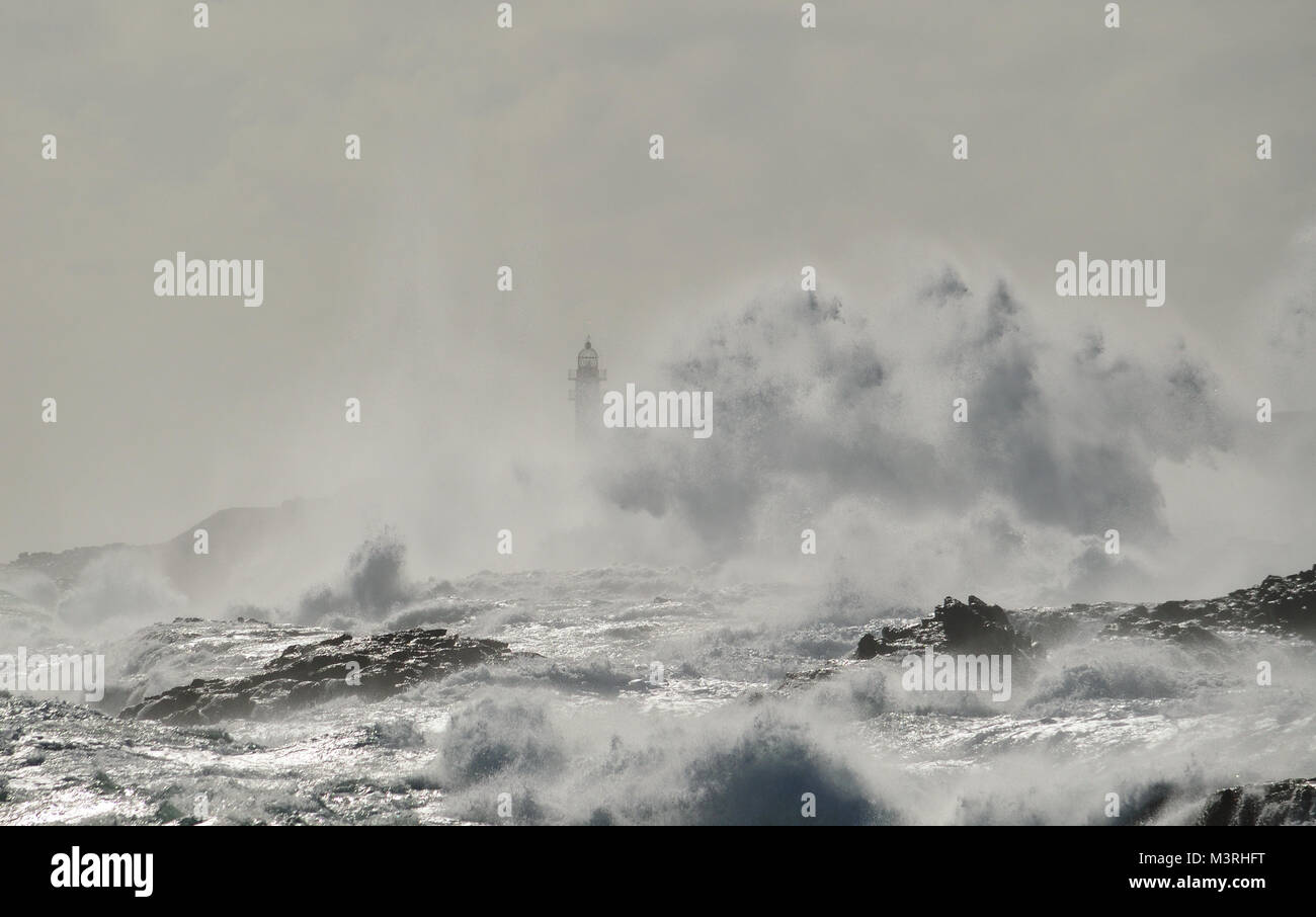 Mare mosso, grande onda quando si rompe sulla costa e silhouette di faro in background, Telde, isole Canarie Foto Stock