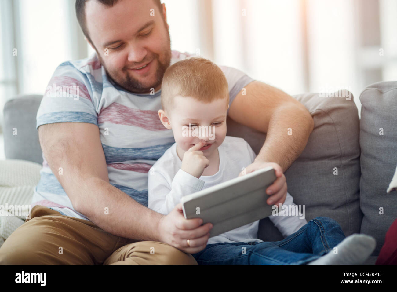 Foto di papà con suo figlio con la compressa seduto sul divano grigio Foto Stock