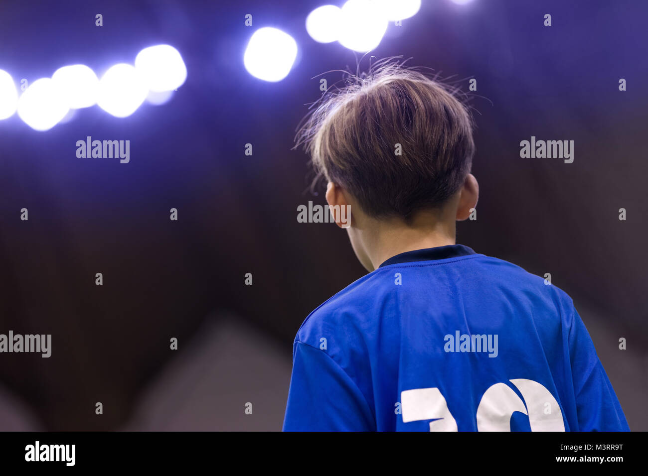 Giovane ragazzo in uno sport jersey. Capretto in blu T-shirt sportiva. Il calcio bambino ritratto. Stadio Sportivo di luci in background. Sport giovanile sullo sfondo Foto Stock