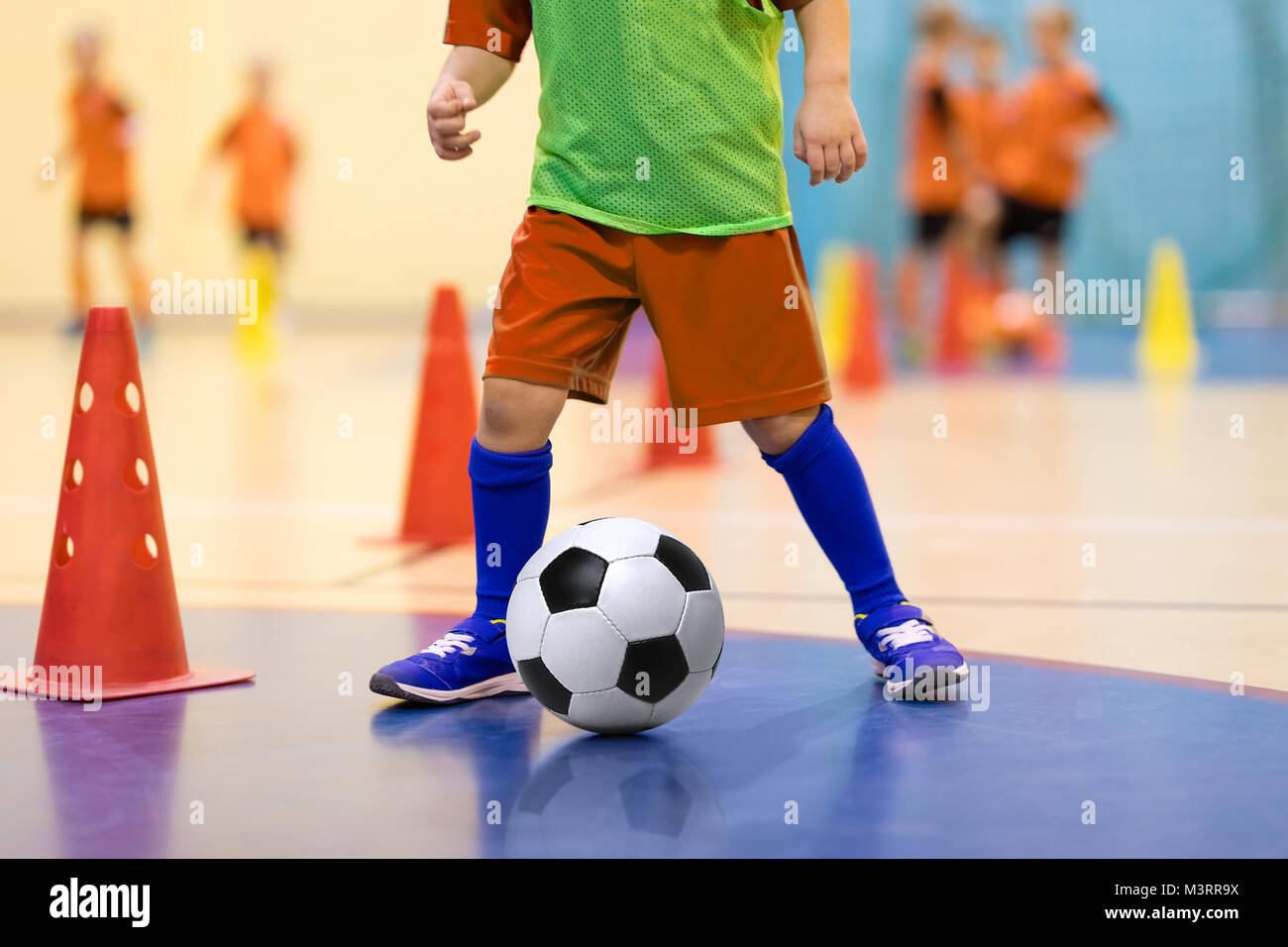 Il calcio futsal formazione per bambini. Allenamento per il calcio dribbling  trapano a cono. Calcetto giovane giocatore con un pallone da calcio in una  sala sportiva. Il giocatore in Foto stock -
