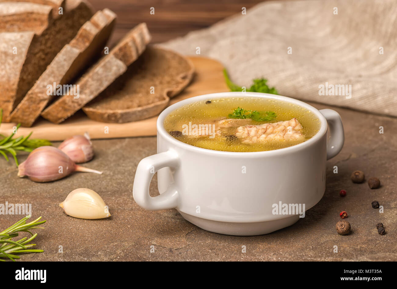 Trasparente fresca zuppa di pesce con lo storione, patate in piastra bianca, decorato di aglio, foglie di prezzemolo e tagliate il pane di segale, mangiare sano Foto Stock