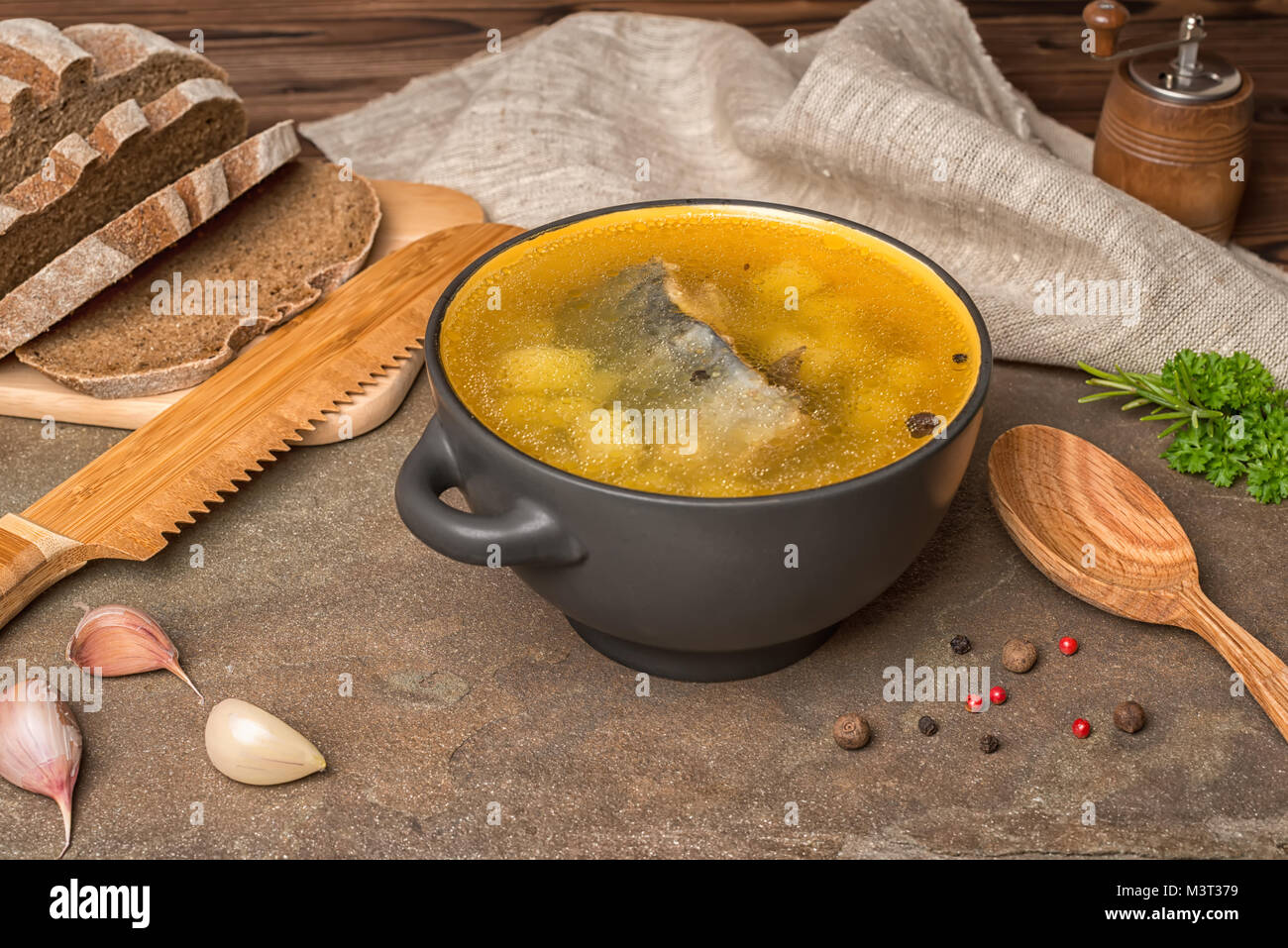 Trasparente fresca zuppa di pesce con lo storione, patate, cipolle e spezie in lamiera nera e pane di segale decorate macinino, tela, la cucina etnica Foto Stock