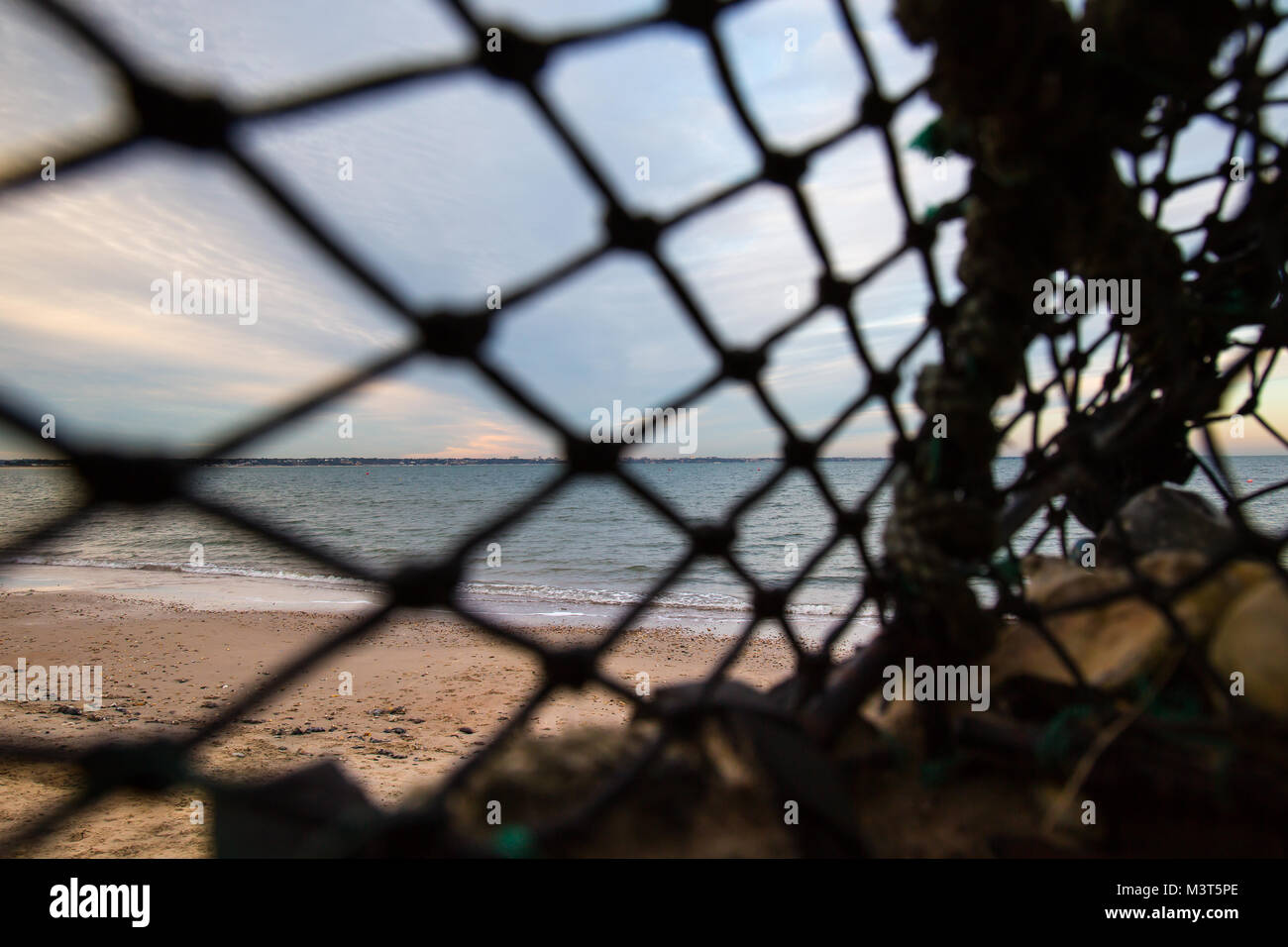 Vista di una spiaggia deserta guardando attraverso il soft-compensazione di messa a fuoco di un vecchio, vuoto, abbandonato Lobster Pot si è incagliata dalla marea. Sunset beachcombing Foto Stock
