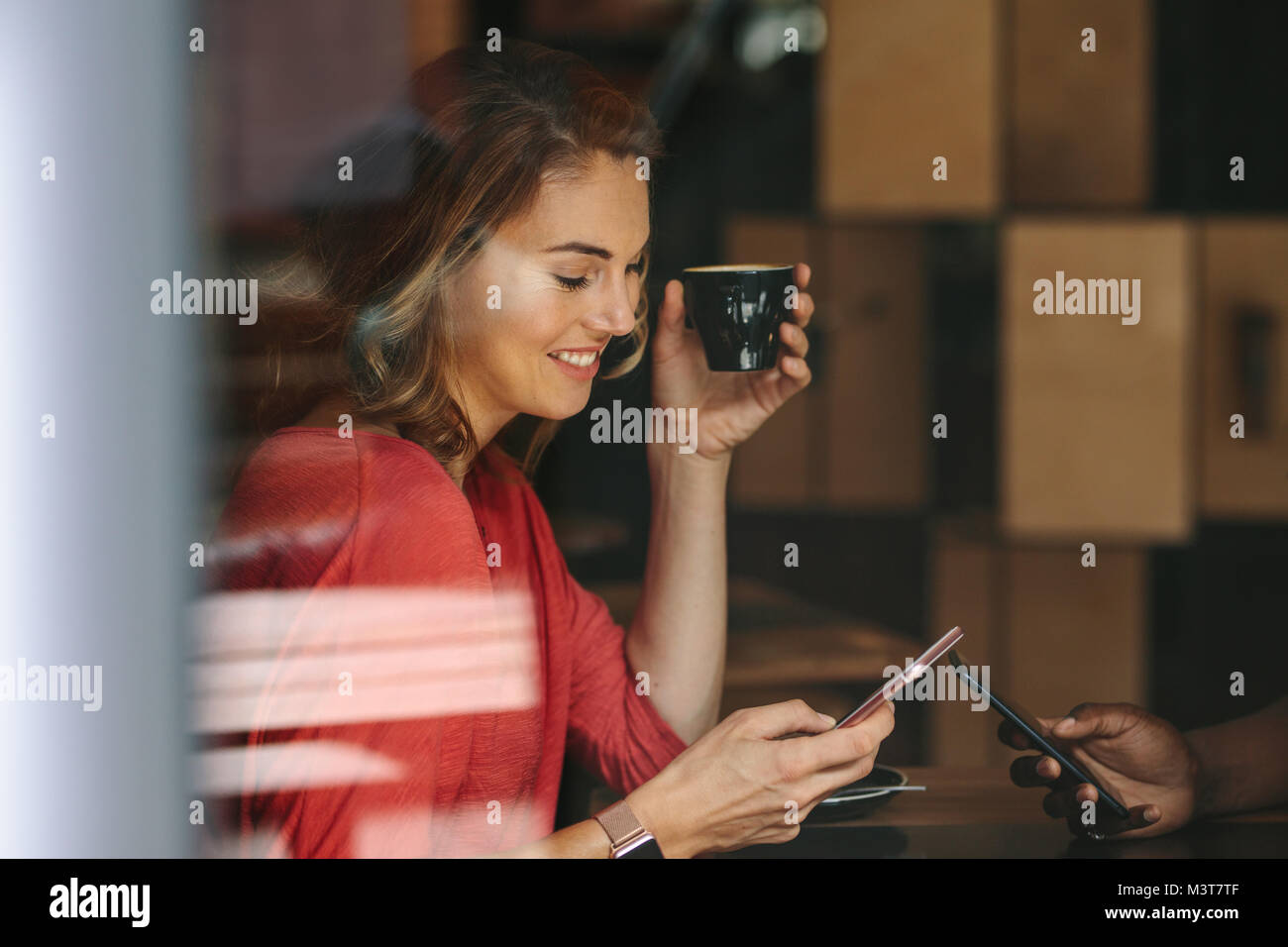 Donna che guarda il suo telefono cellulare mentre si tiene una tazza di caffè. Donna sorridente incontro con il suo amico in una caffetteria. Foto Stock
