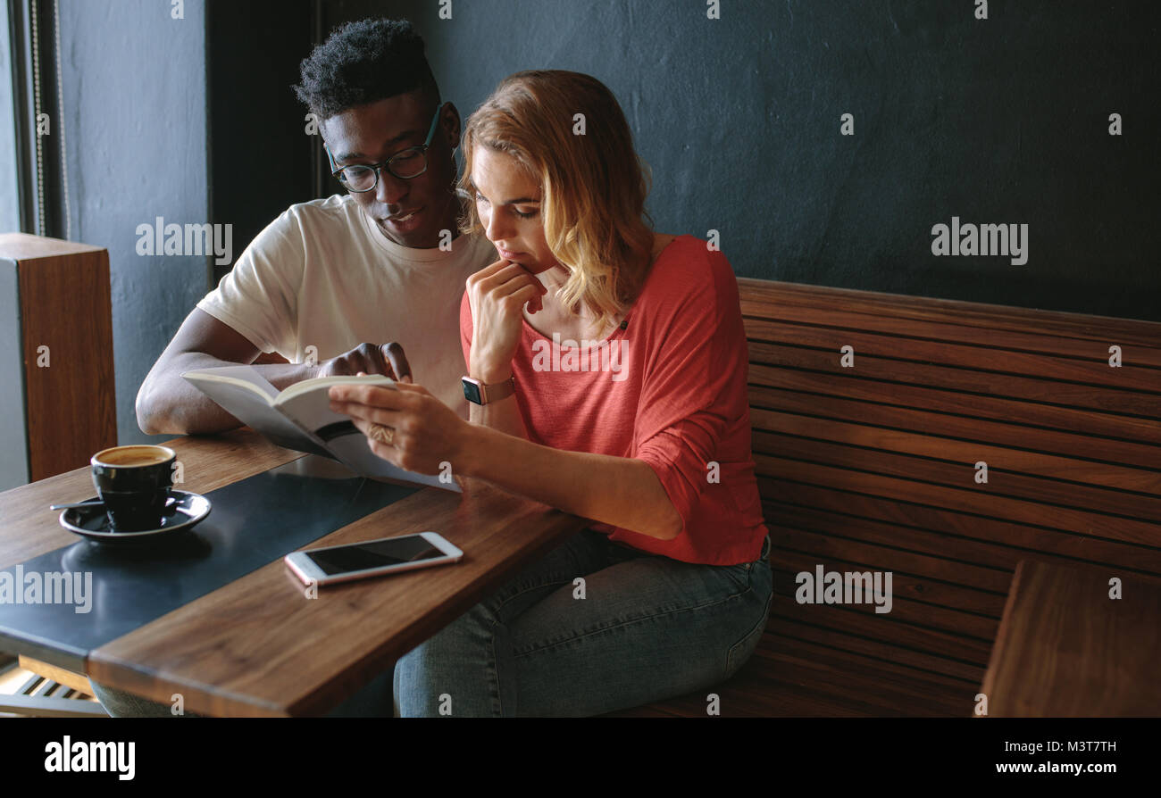 L uomo e la donna seduta al tavolo da caffè la lettura di un libro insieme. Matura in un coffee shop la lettura di un libro con una tazza di caffè sul tavolo. Foto Stock