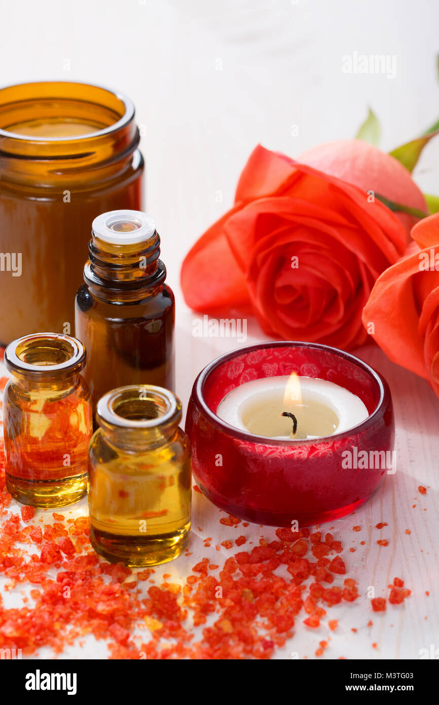 Olio essenziale di minerali, sali da bagno, candela e fiori sul tavolo di legno. Foto Stock