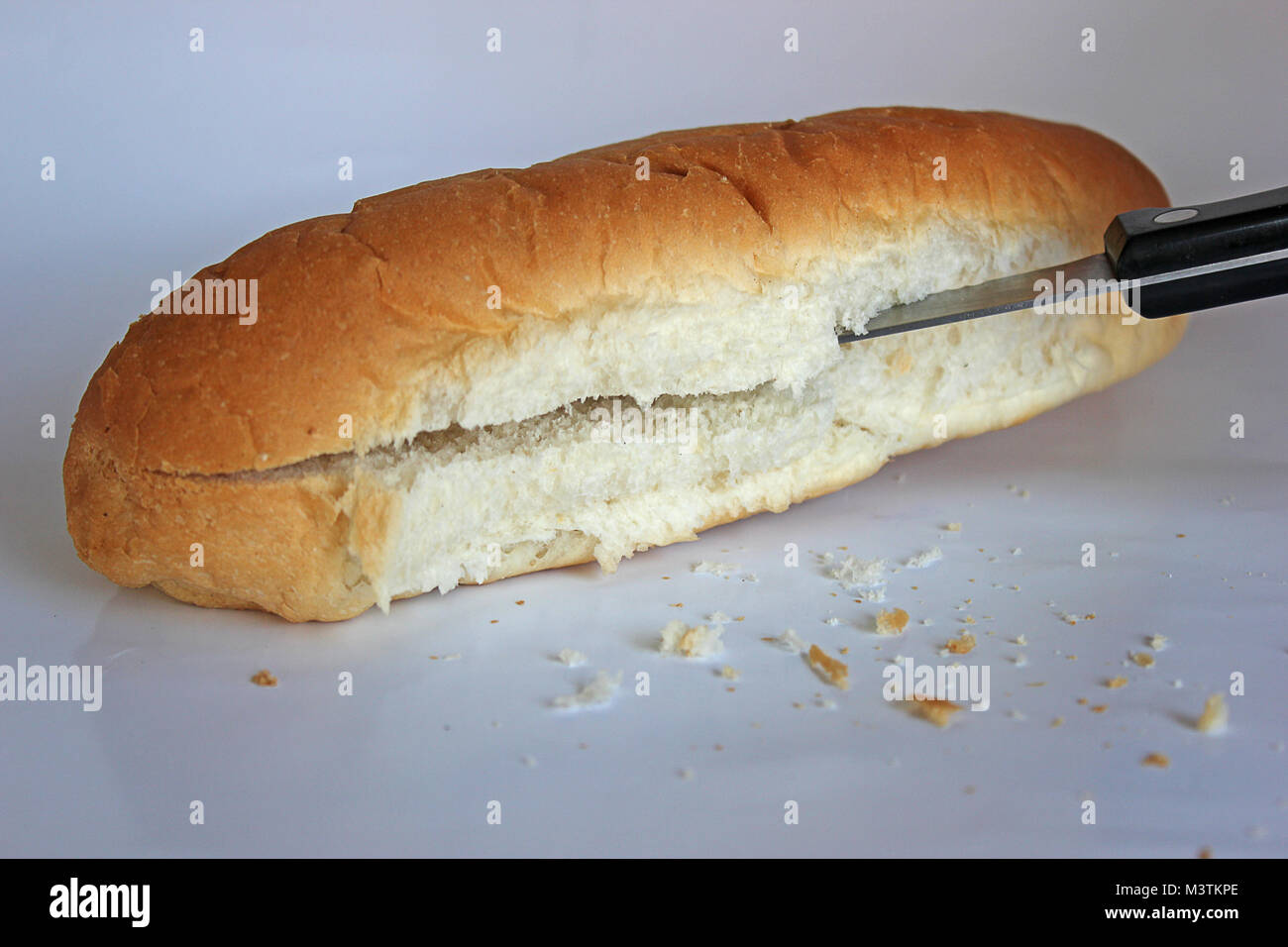 Hot Dog bun o un piccolo pezzo di pane tagliato con Coltello per pane su sfondo chiaro con le briciole che giace nella parte anteriore Foto Stock