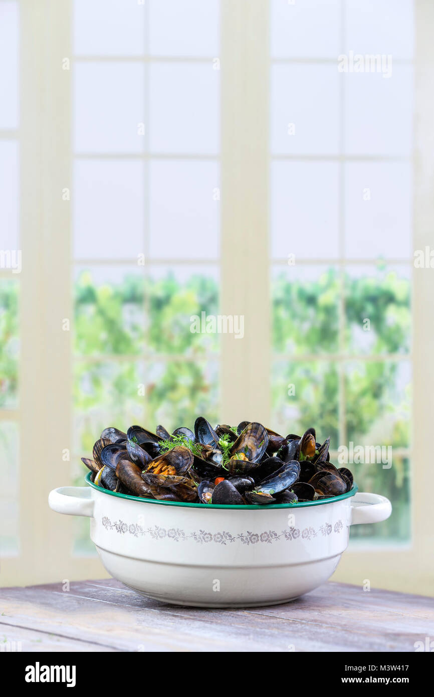 Cucinato blu francese le cozze con il prezzemolo nel vecchio vintage pot di smalto su una cucina di sfondo di Windows Foto Stock