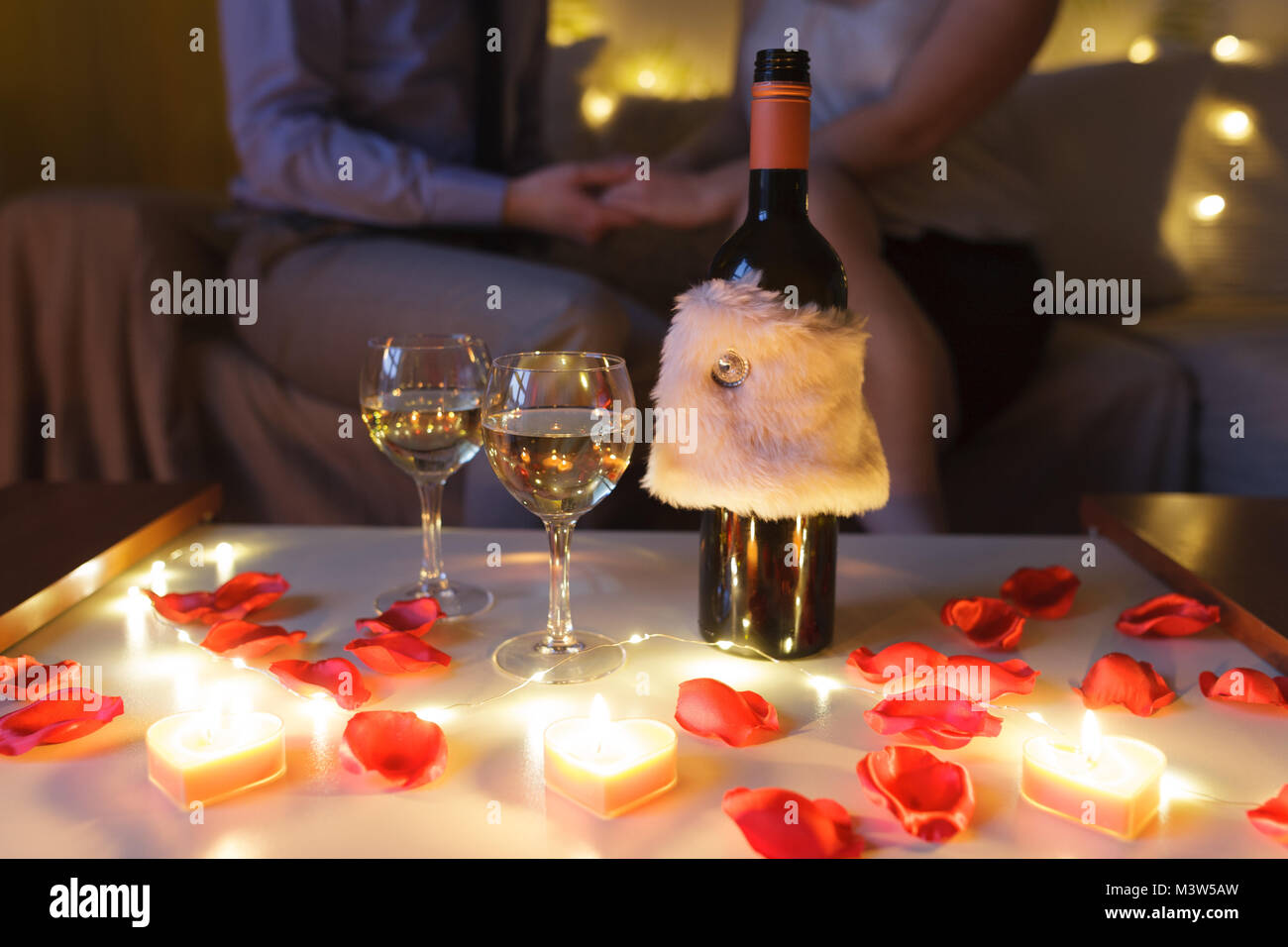 ​Couple in amore sul divano per celebrare il giorno di San Valentino a casa di notte. Focus sul tavolo con bicchieri di vino e di dono. Foto Stock