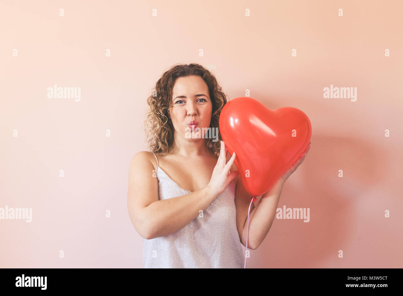 Ricci ​Beautiful giovane donna in possesso di una forma di cuore pallone aerostatico sul colore di sfondo. Il giorno di San Valentino concetto, simbolo dell'amore. Foto Stock