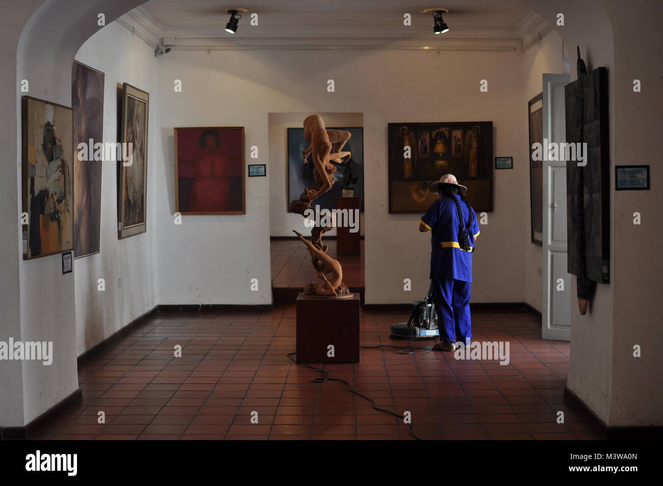 Un latino-americano cleaner Vestito in blu la pulizia del pavimento di una galleria d'arte Foto Stock