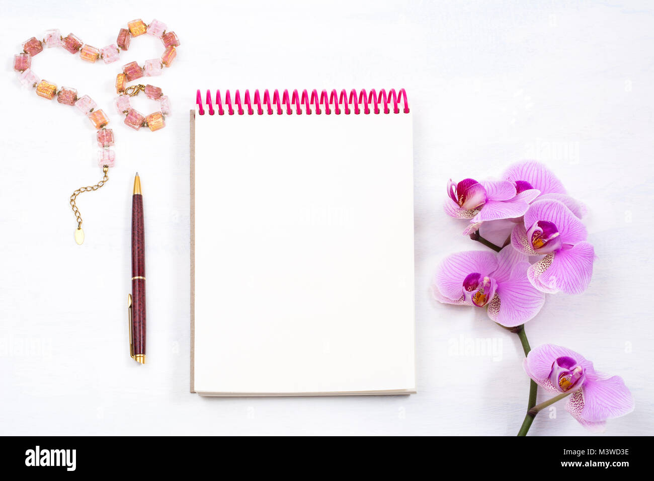 Area di lavoro femminile mockup con il blocco note e penna e orchidea rosa su sfondo bianco, vista dall'alto Foto Stock