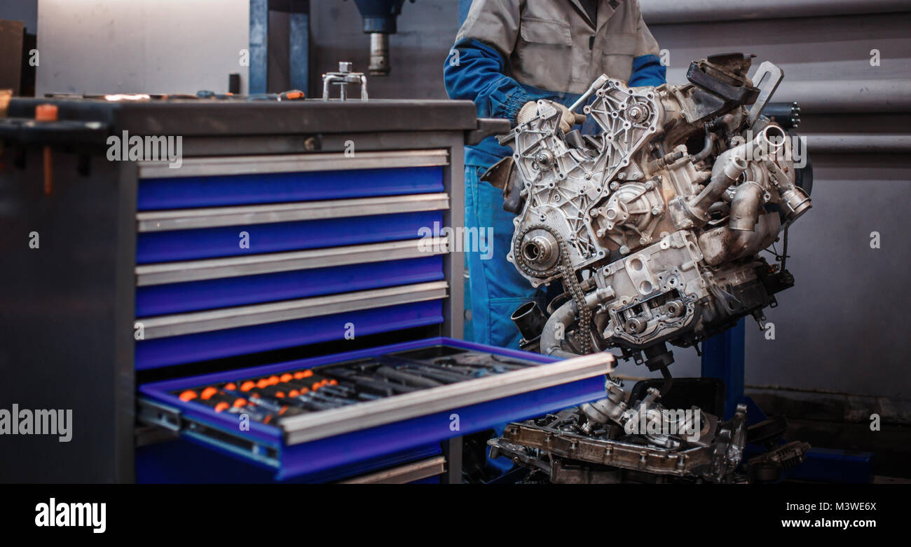 Revisionare la riparazione. Il giovane meccanico automatico smantella il motore di contrasto per la diagnosi e la riparazione presso lo stand in officina. Foto Stock