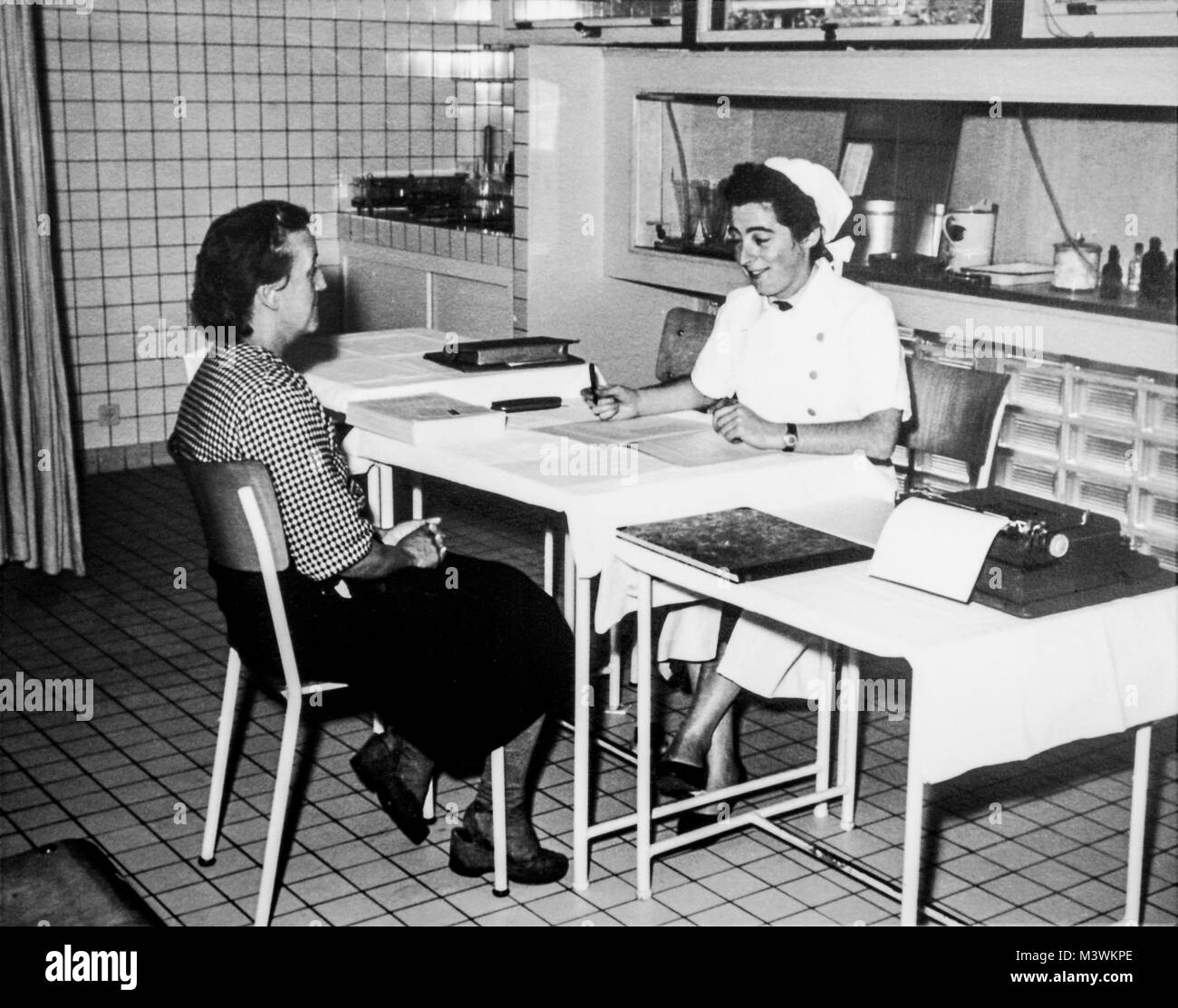 Il vecchio bianco e nero fotografia archivio mostra femmina operaio di fabbrica visitando infermiere al dispensario negli anni cinquanta Foto Stock