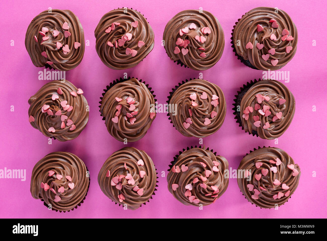 Colorato tortini di cioccolato con cuore conformato spruzza su un sfondo rosa. Pattern Foto Stock