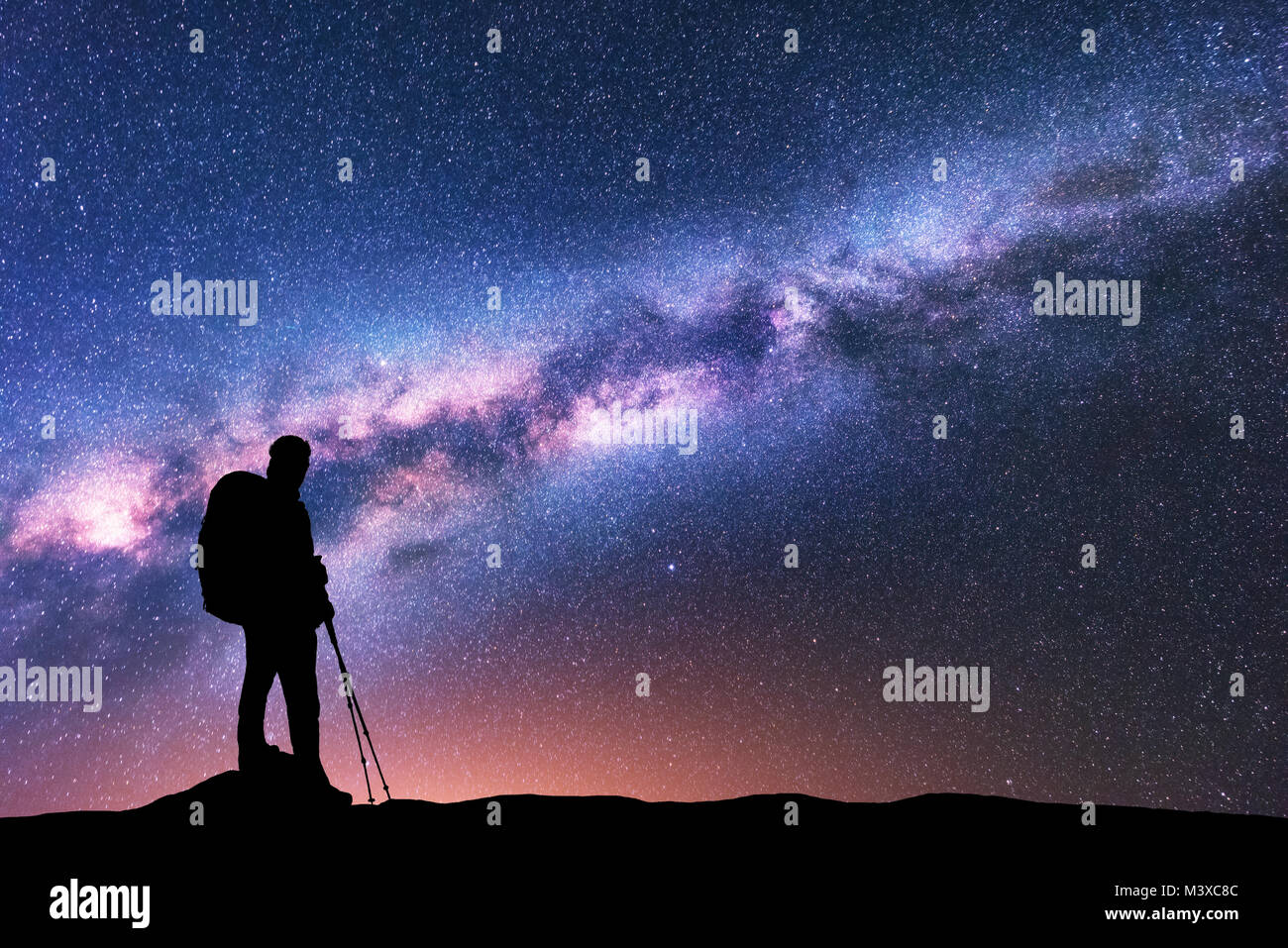 Silhouette di uomo con zaino e bastoncini da trekking contro incredibile viola via lattea di notte. Spazio. Paesaggio con uomo, brillante Via Lattea, sky con st Foto Stock